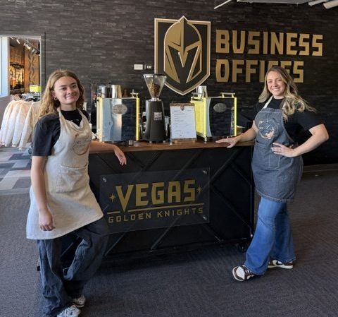 Two girls standing in front of a coffee bar with aprons on