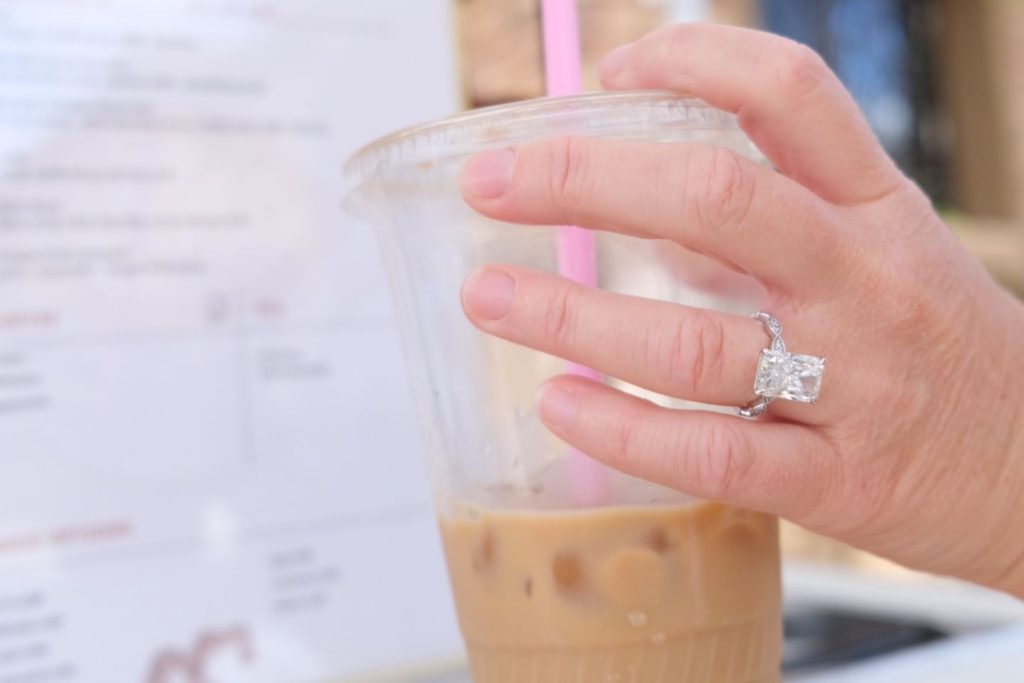 hand with engagement ring holding iced coffee beverage