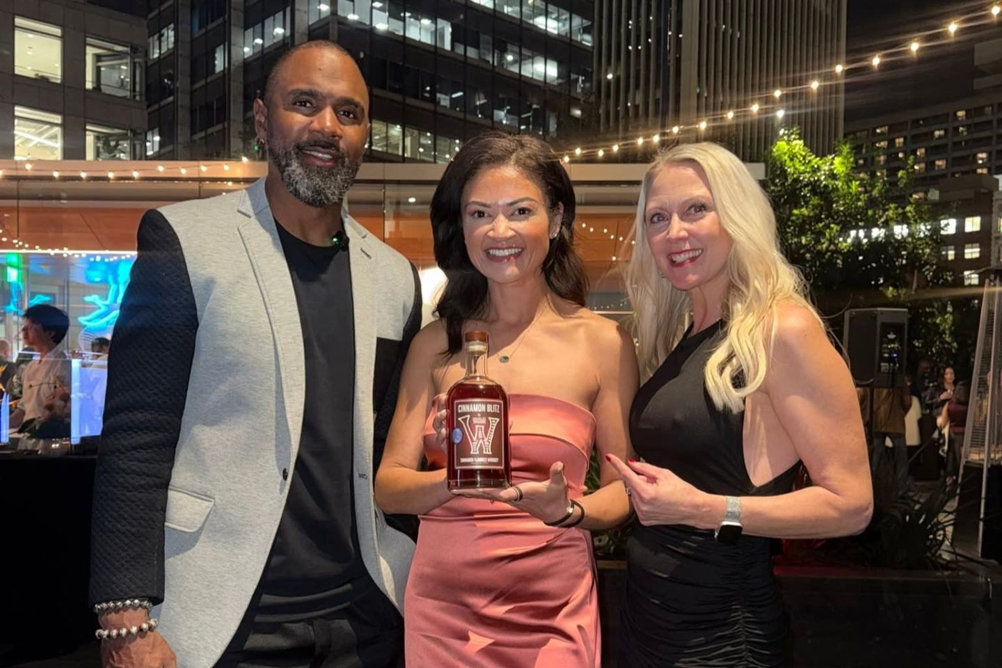 Three people standing together at a fancy event one in middle is holding whisky